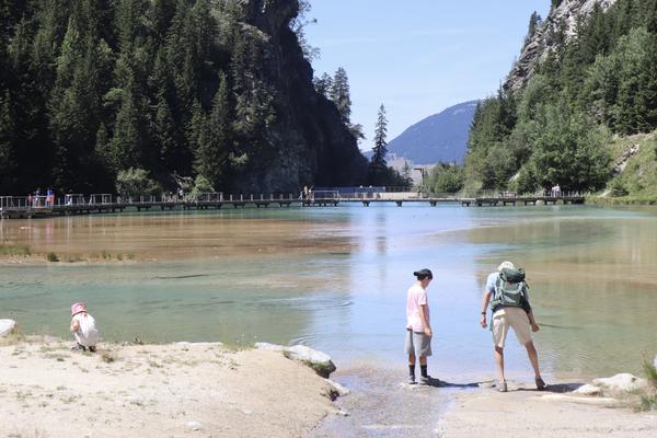 The photo captures a serene summer day at a mountain lake, where several people are enjoying the clear weather